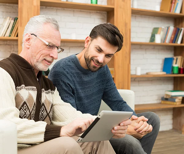 hombre-envejecido-joven-sonriente-tableta-sofa